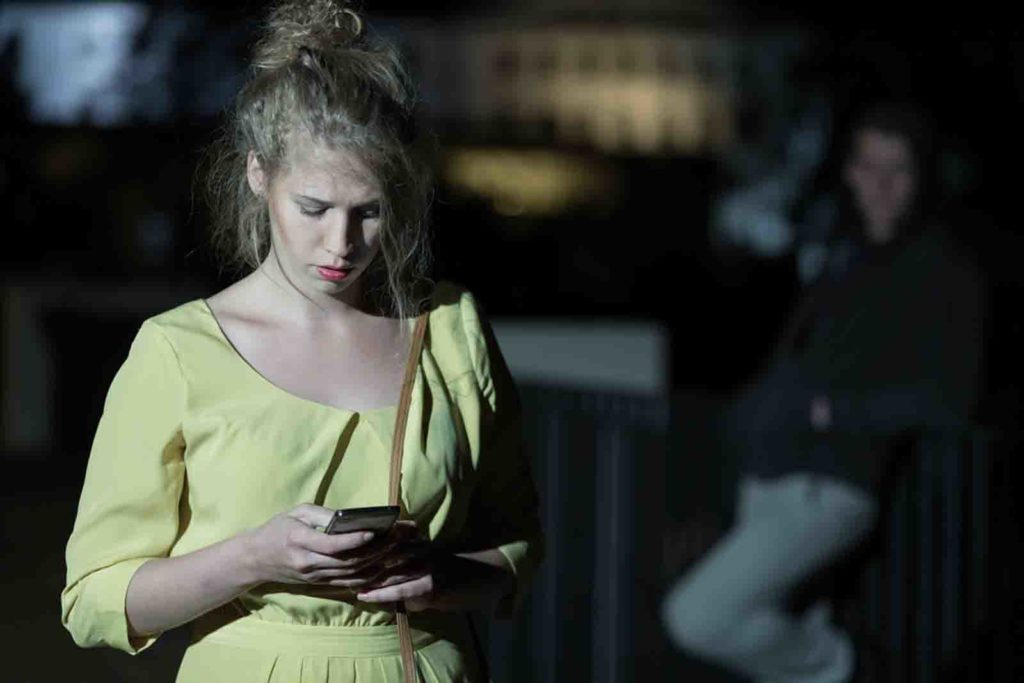 Woman with mobile phone walking alone at night